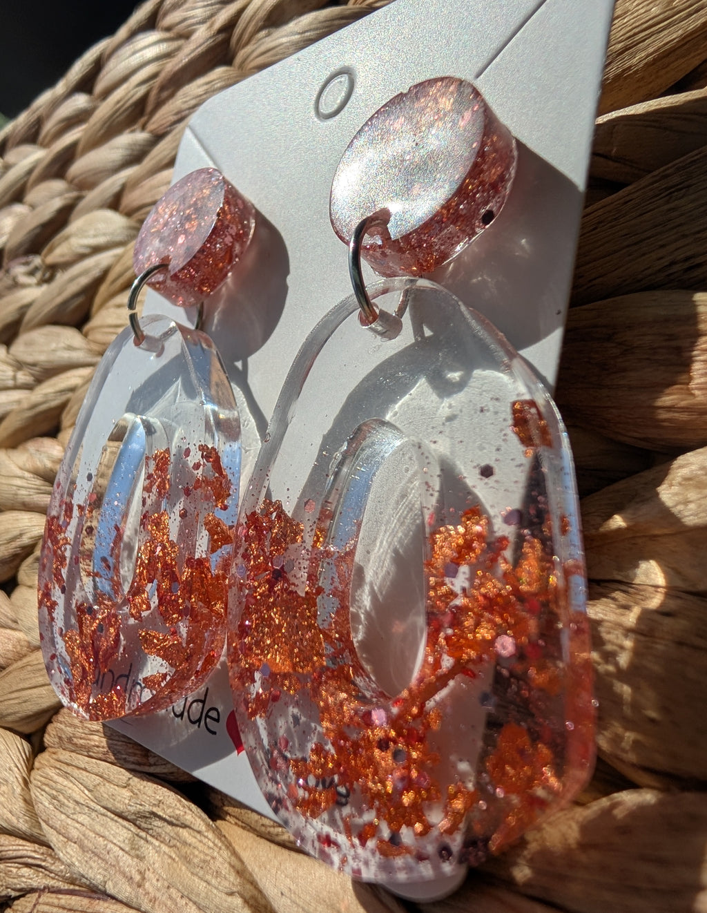 Earrings with orange and clear design on a woven surface